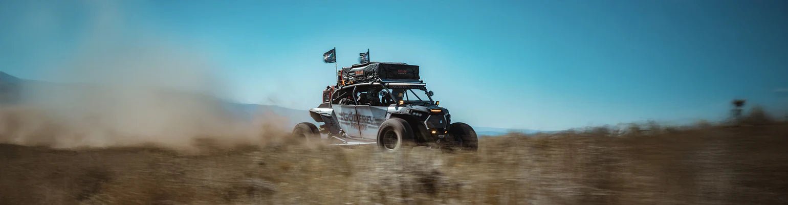 Polaris RZR driving on a dirt road with a clear blue sky overlanding